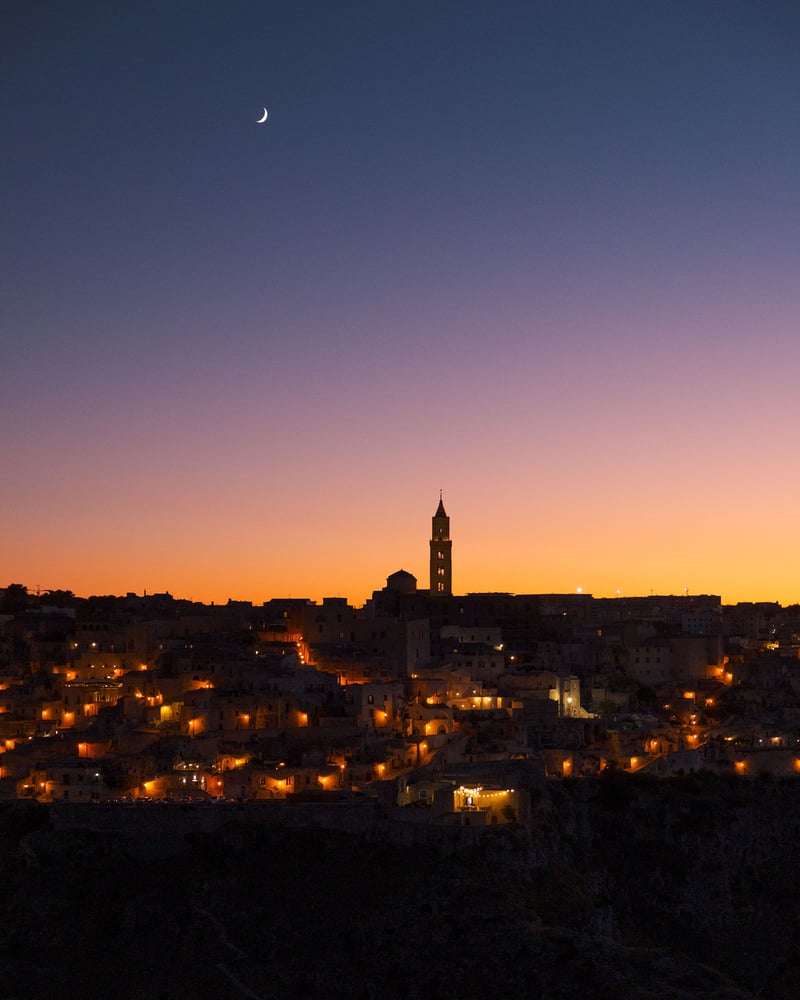 The moon setting after the sun behind the Sassi of Matera.