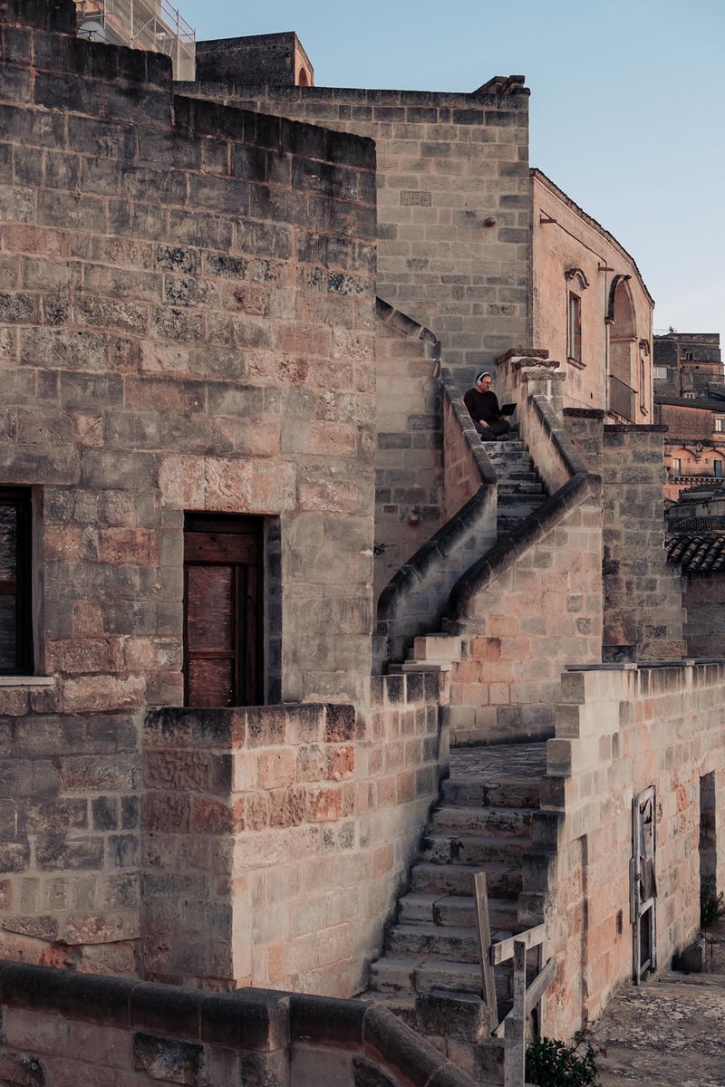 A man working remotely sitting on the top of a staircase in the Sassi of Matera.
